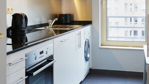 A modern kitchen with white cabinets, a built-in oven, a coffee maker, and a window with a view of buildings. - Thon Residence Parnasse (Brussels)