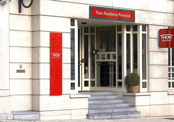 Entrada de un edificio con un letrero que dice 'Thon Residence Parnasse' y una planta en maceta en los escalones.