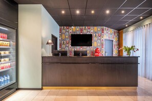 A reception desk with a flat-screen TV, a Coca-Cola refrigerator, and a water dispenser. - Thon Residence Parnasse (Brussels)
