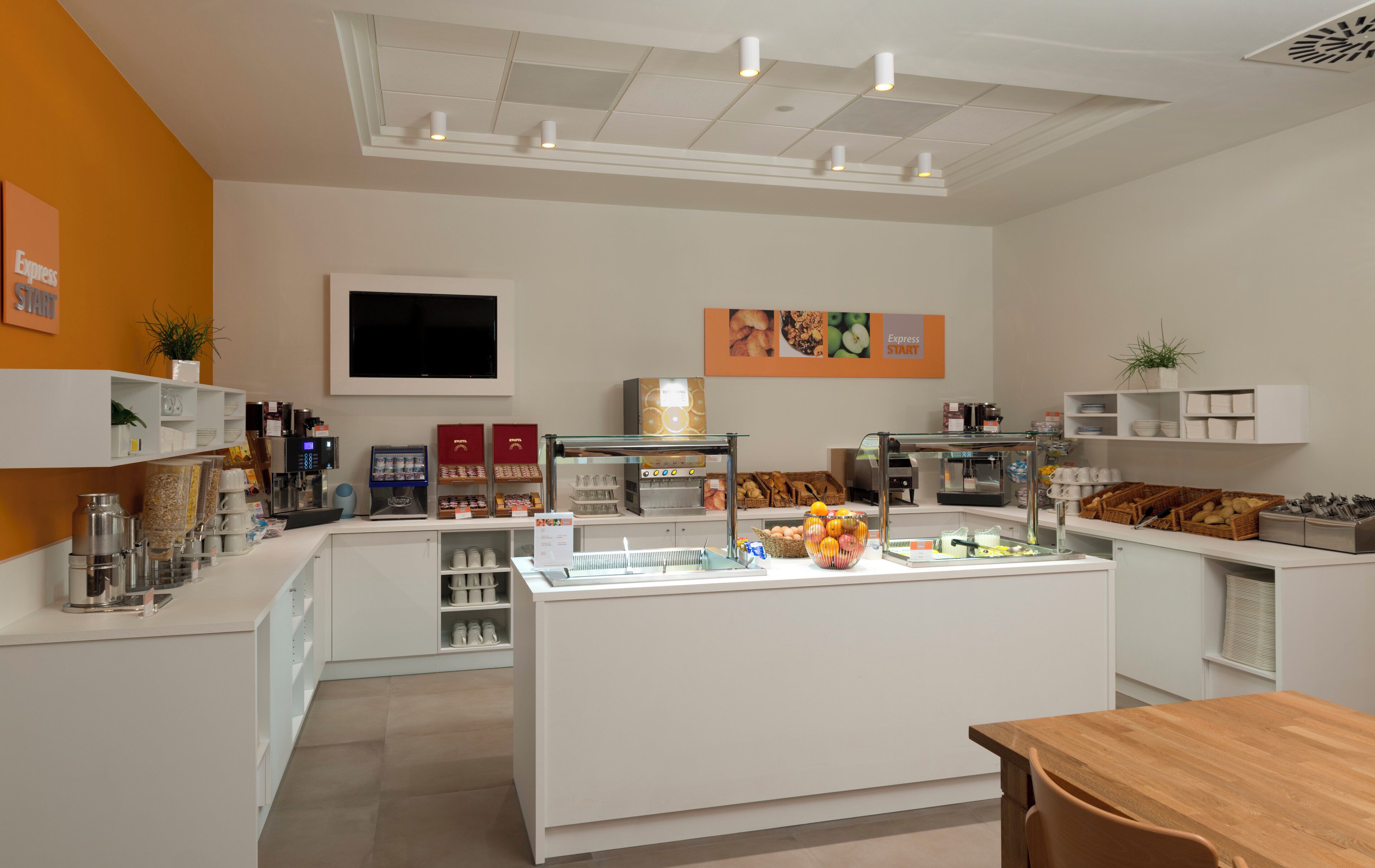 A modern cafe with a central counter, coffee machines, and a variety of food items.