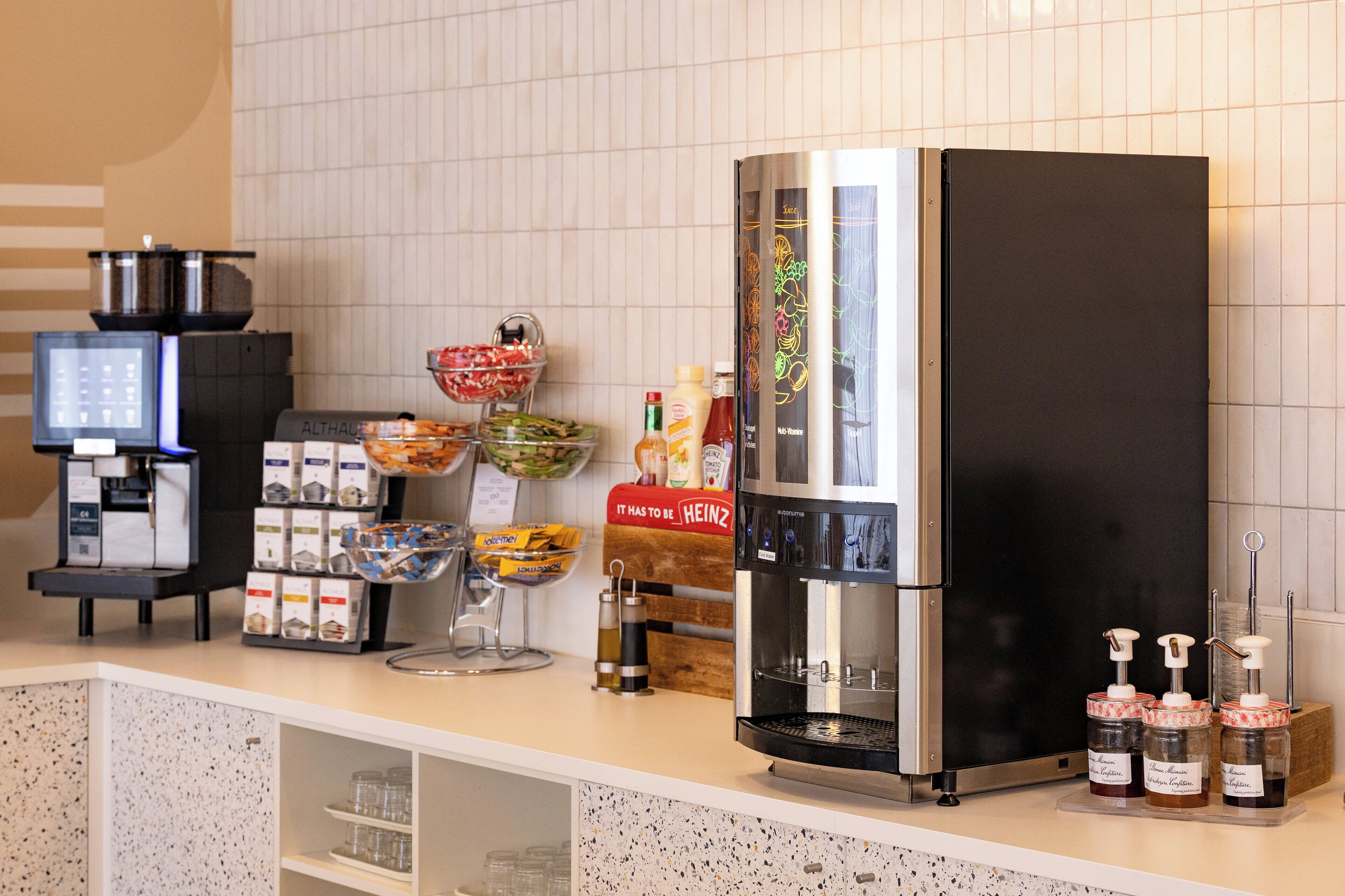 Een koffiehoek met een koffieapparaat, dispensers voor toevoegingen en diverse koffiekapsules en melkflessen.