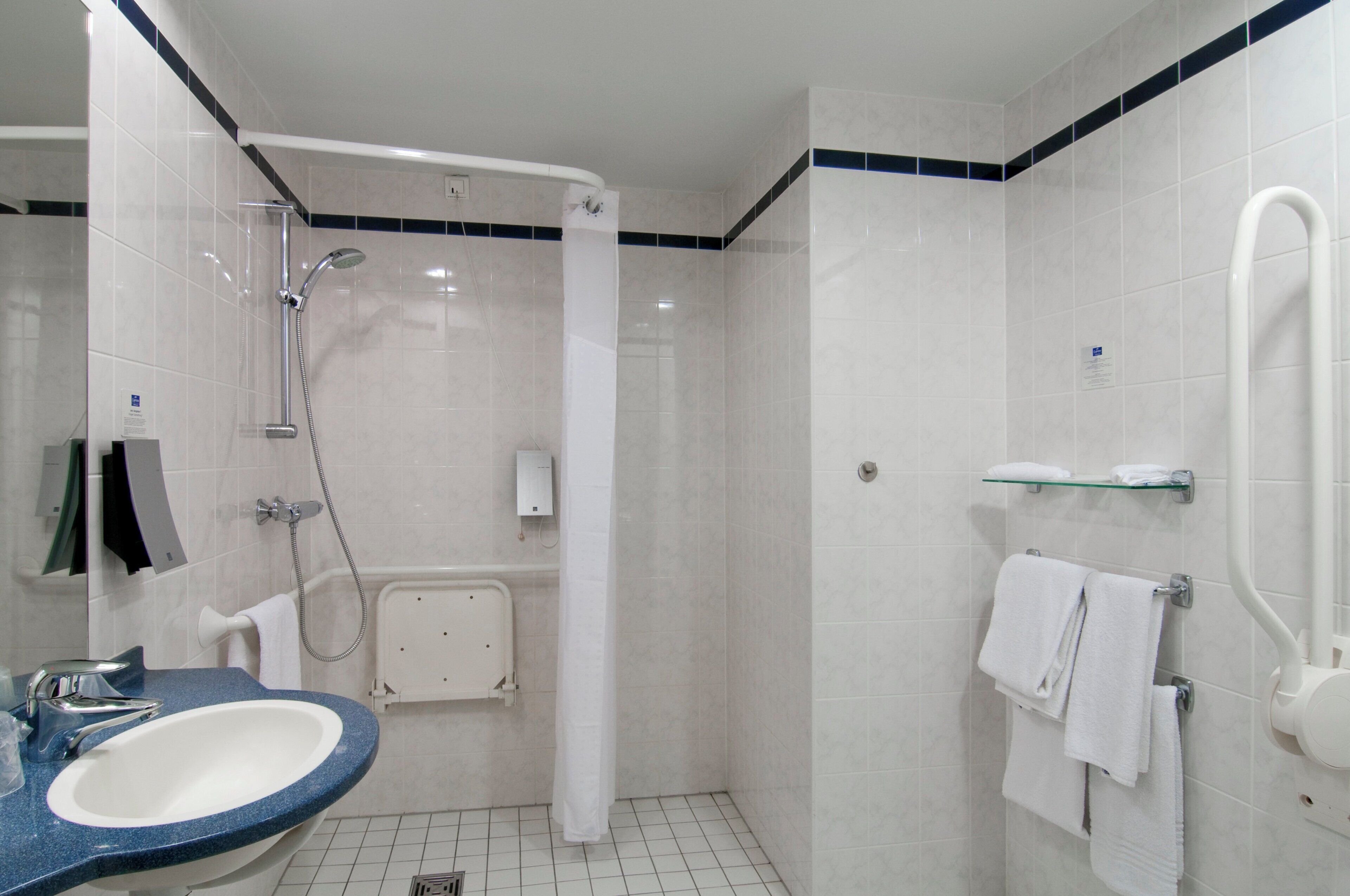 A bathroom with a shower, a sink, and a glass shelf.