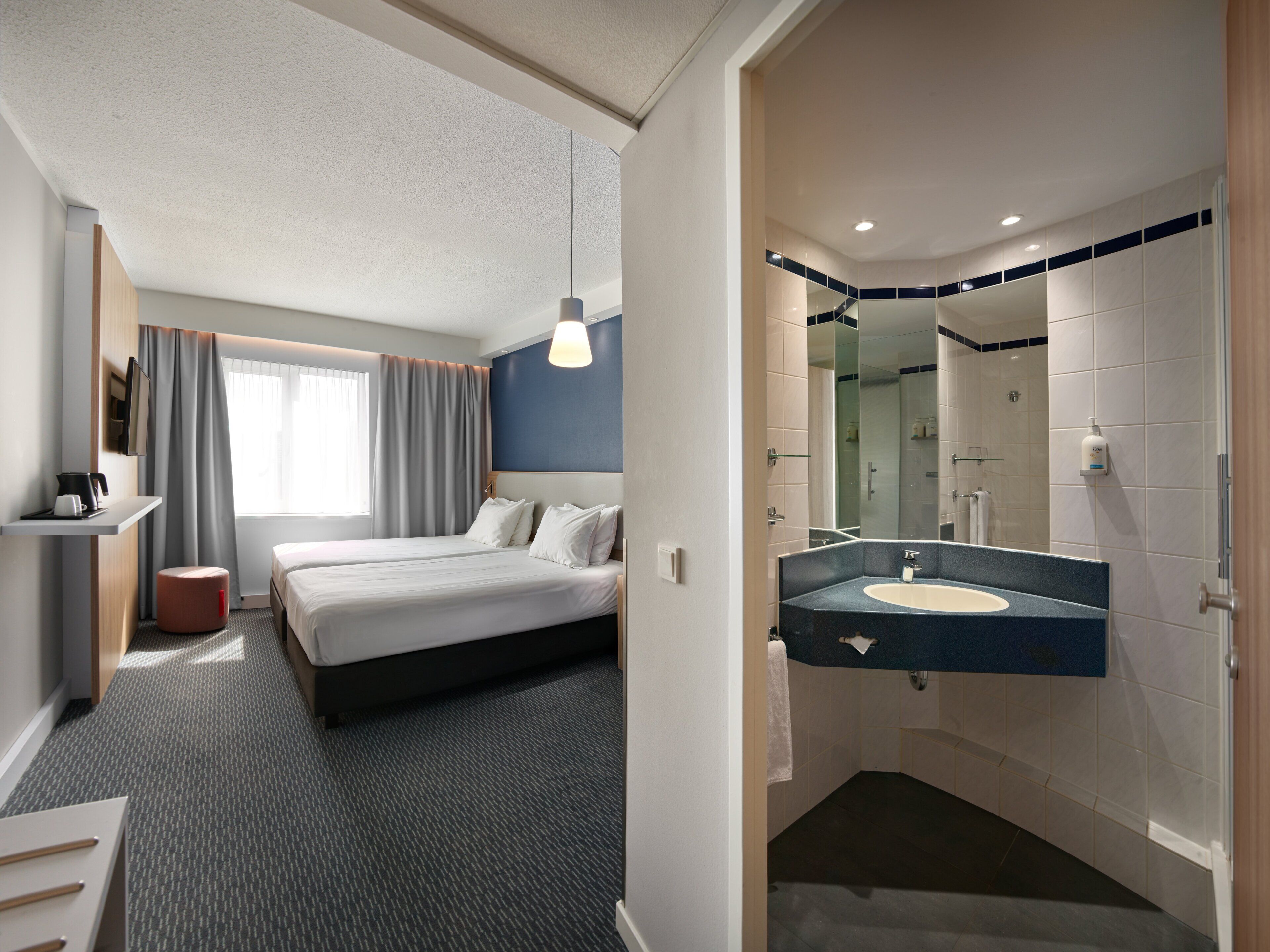 A hotel room with a bed, bedside table, and a bathroom with a sink and mirror.