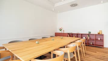 A conference room with a long wooden table, multiple chairs, a red bookshelf, and a white wall.