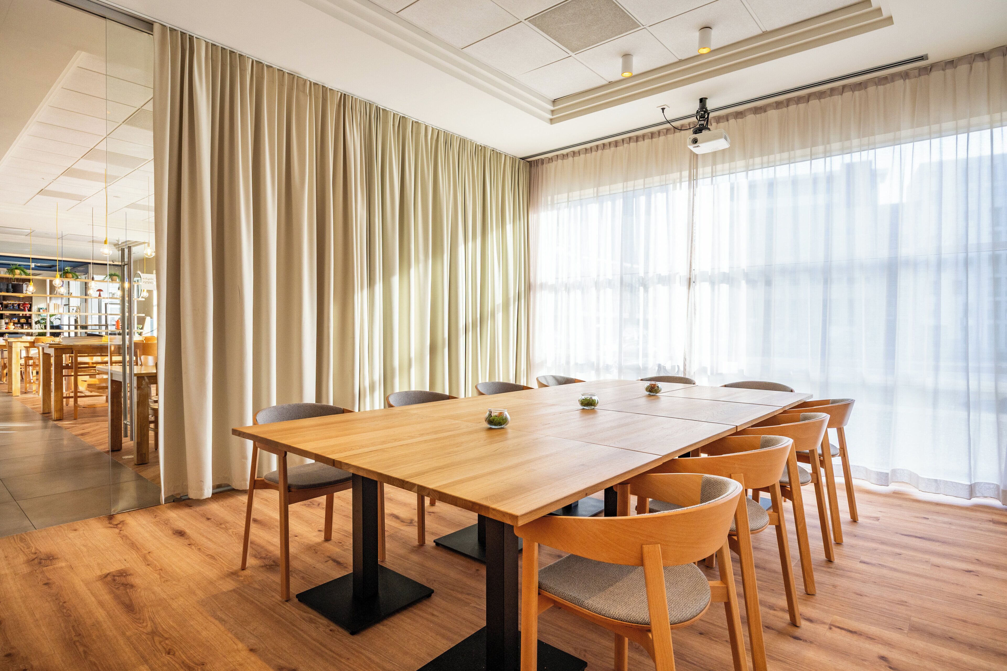 Una sala de conferencias con una mesa de madera, sillas y un amplio ventanal con cortinas.