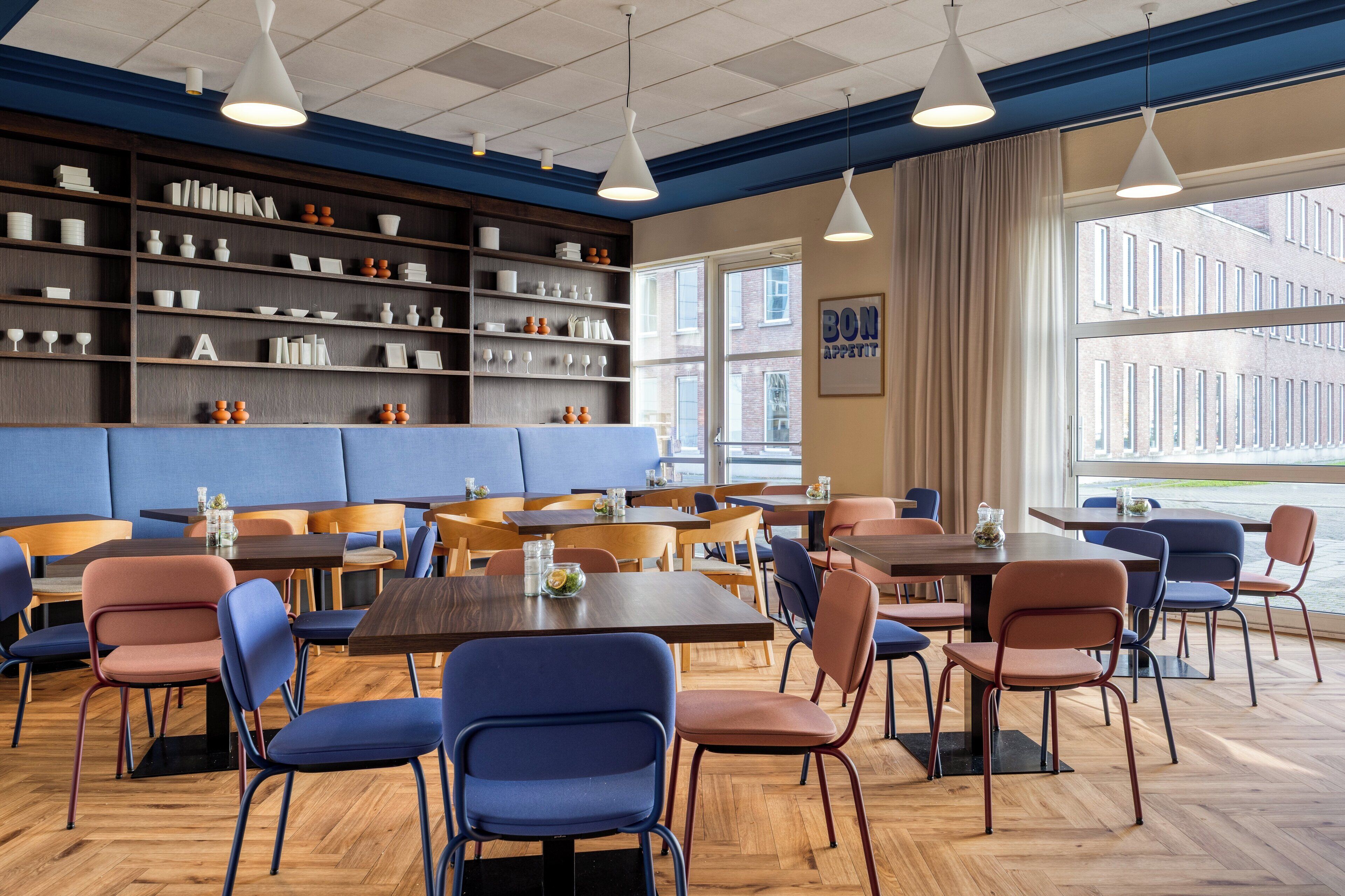 A modern dining area with wooden tables and blue chairs, a blue cushioned bench, and shelves with dishes and glasses.