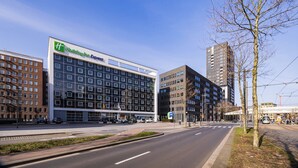 A modern building with a Holiday Inn Express sign, a large parking lot, and a tram line. - Holiday Inn Express Antwerp City-North by IHG (Antwerp)