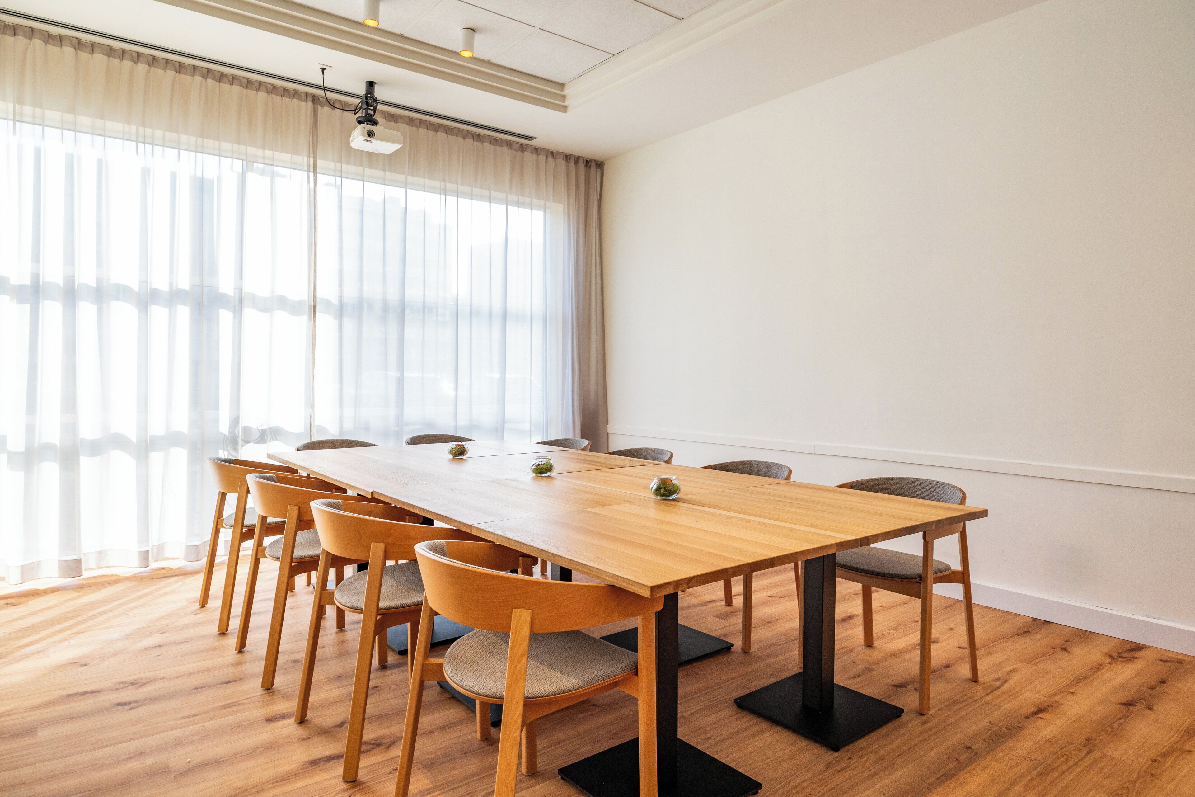 A conference room with a wooden table, chairs, and a large window with sheer curtains.