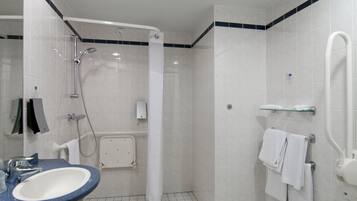 Un baño moderno con ducha, lavamanos y un estante de vidrio con toallas.