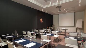 A conference room with tables, chairs, a projector screen, and a large portrait on the wall.