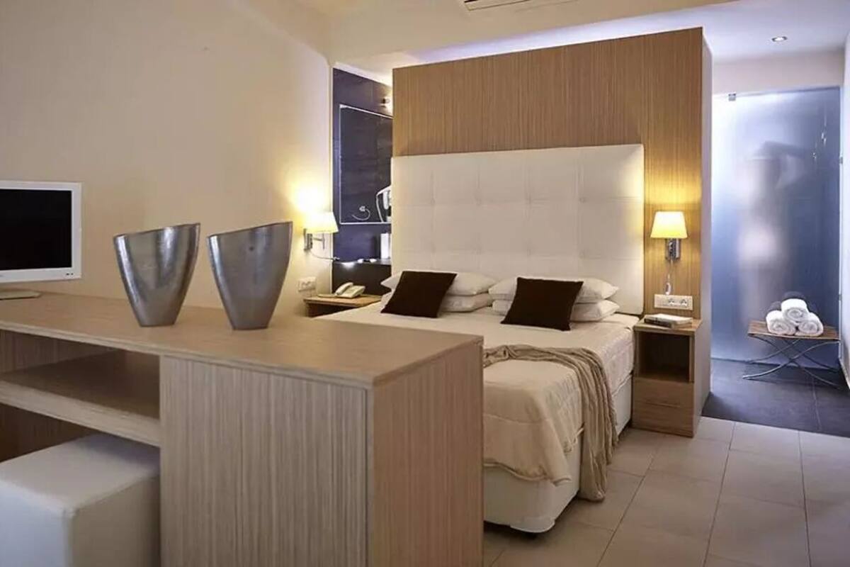 A modern hotel room with a bed, bedside tables, a TV, and a desk with decorative items.