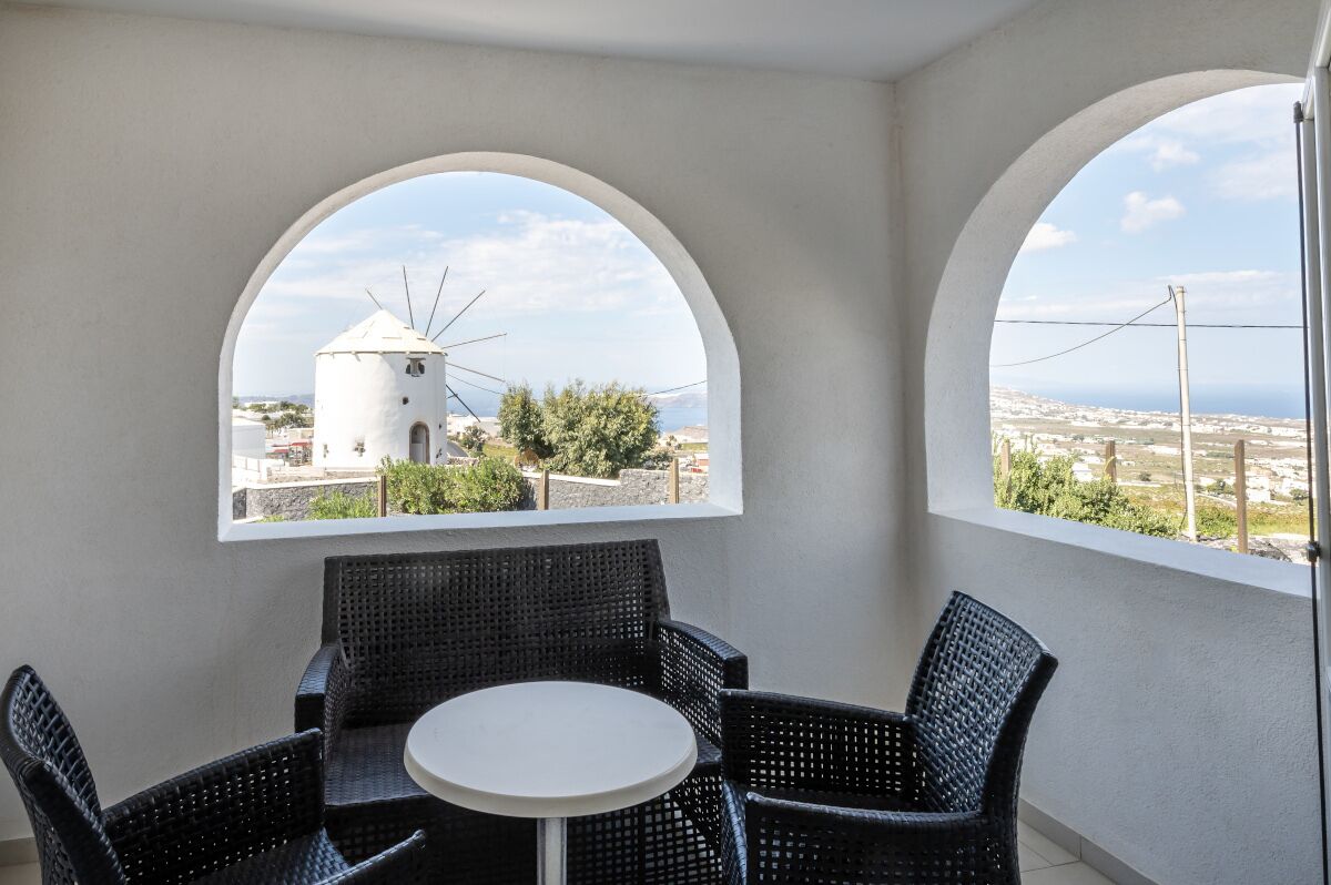 Een balkon met twee rondboogvensters, rieten meubilair en uitzicht op een witte toren en stadsbeeld.