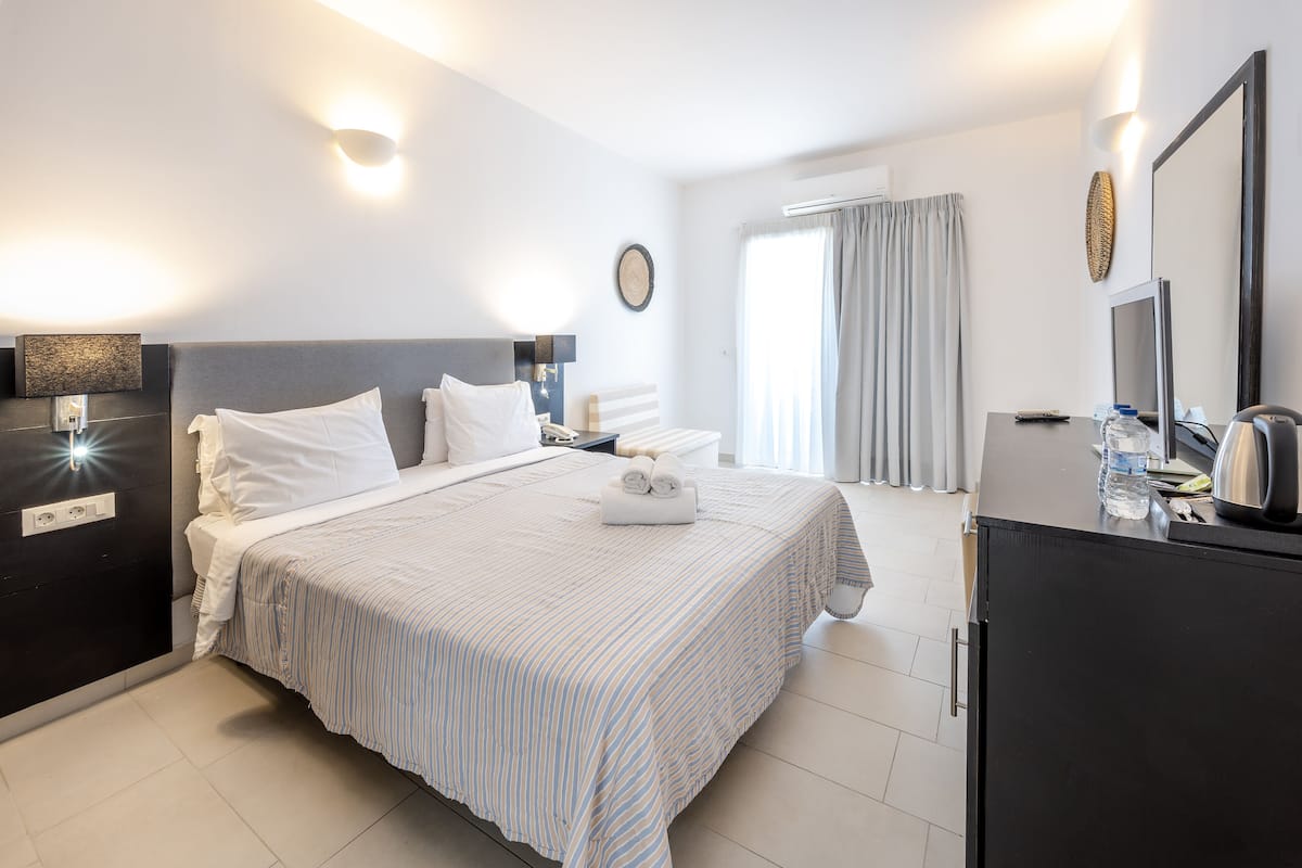 A modern hotel room with a large bed, bedside tables, a flat-screen TV, and a minibar.