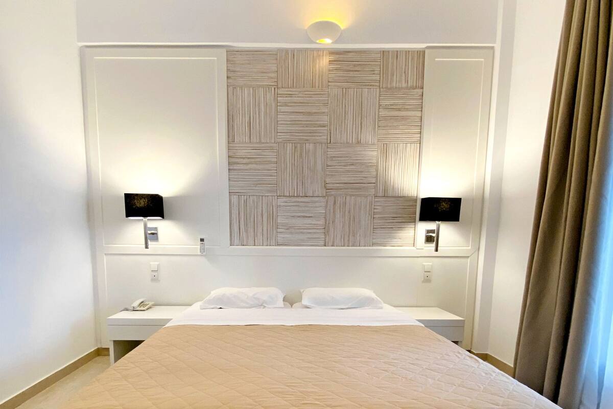 A hotel room with a large bed, two bedside tables, a wall-mounted light fixture, and a curtain on the window.