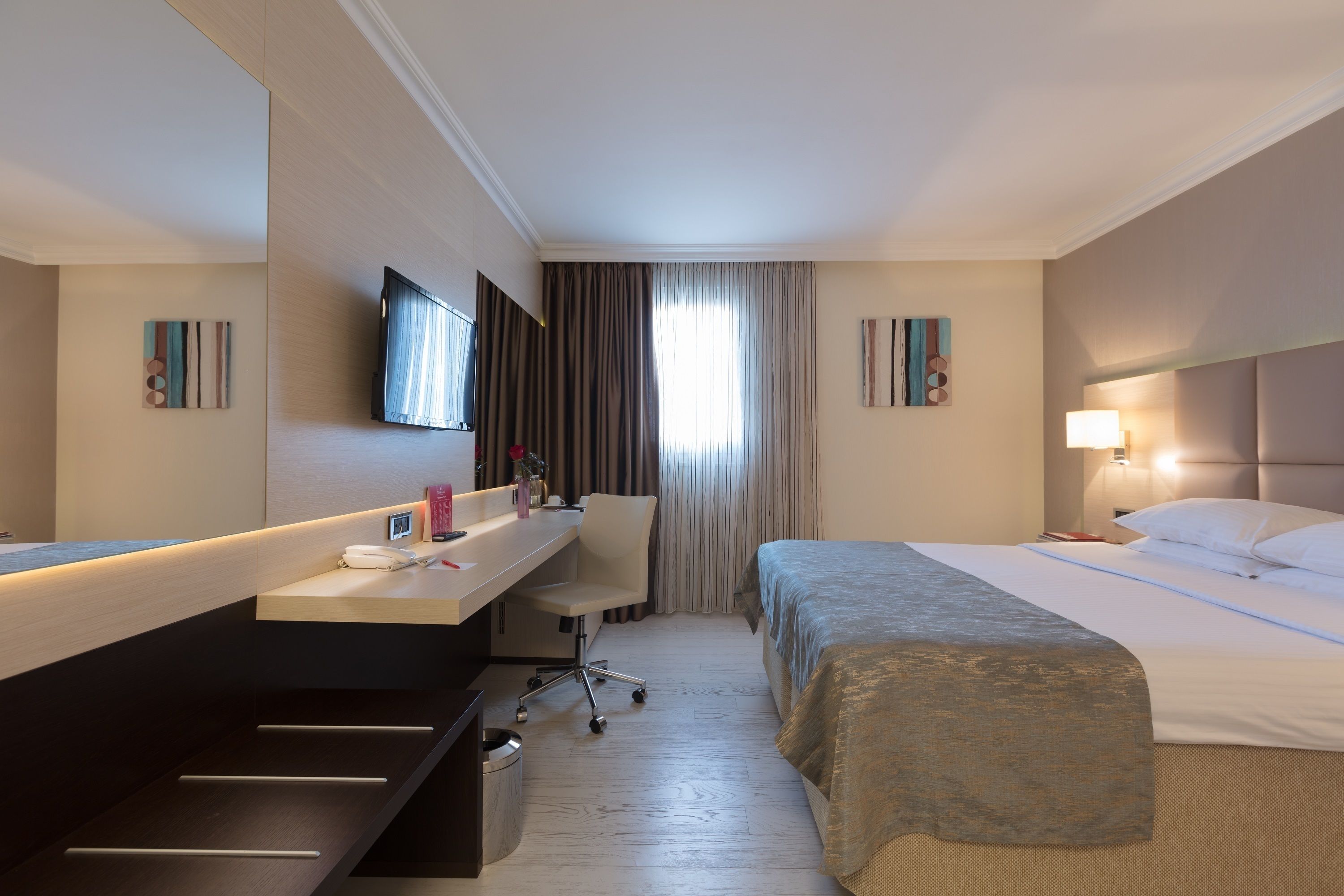 A hotel room with a bed, a desk, a chair, a TV, and a window with curtains.