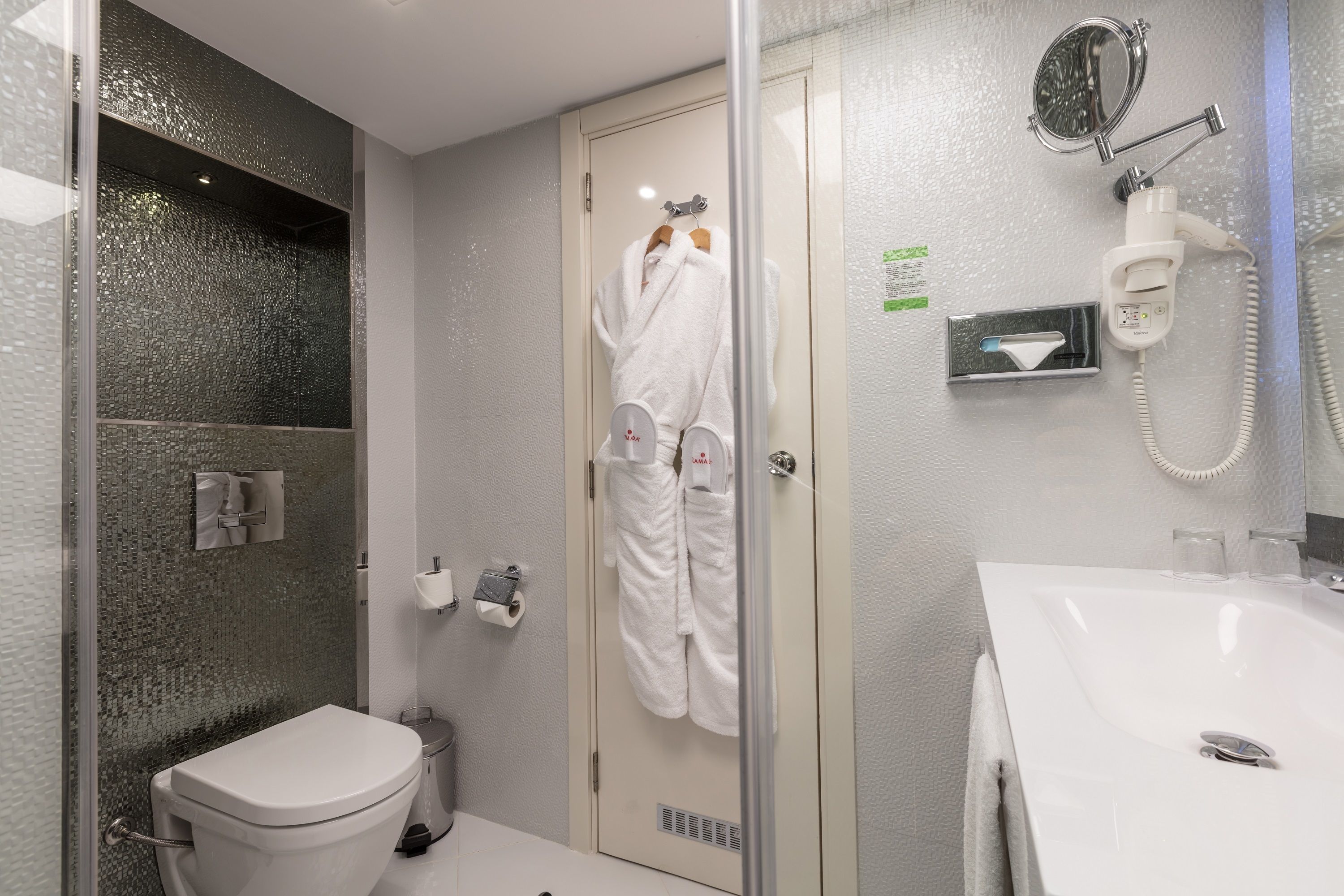 Un baño con inodoro, cabina de ducha de vidrio, lavamanos y perchero para toallas.