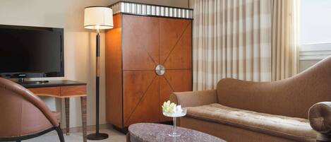 Una habitación de hotel con televisor, sofá, sillón, mesita y lámpara.