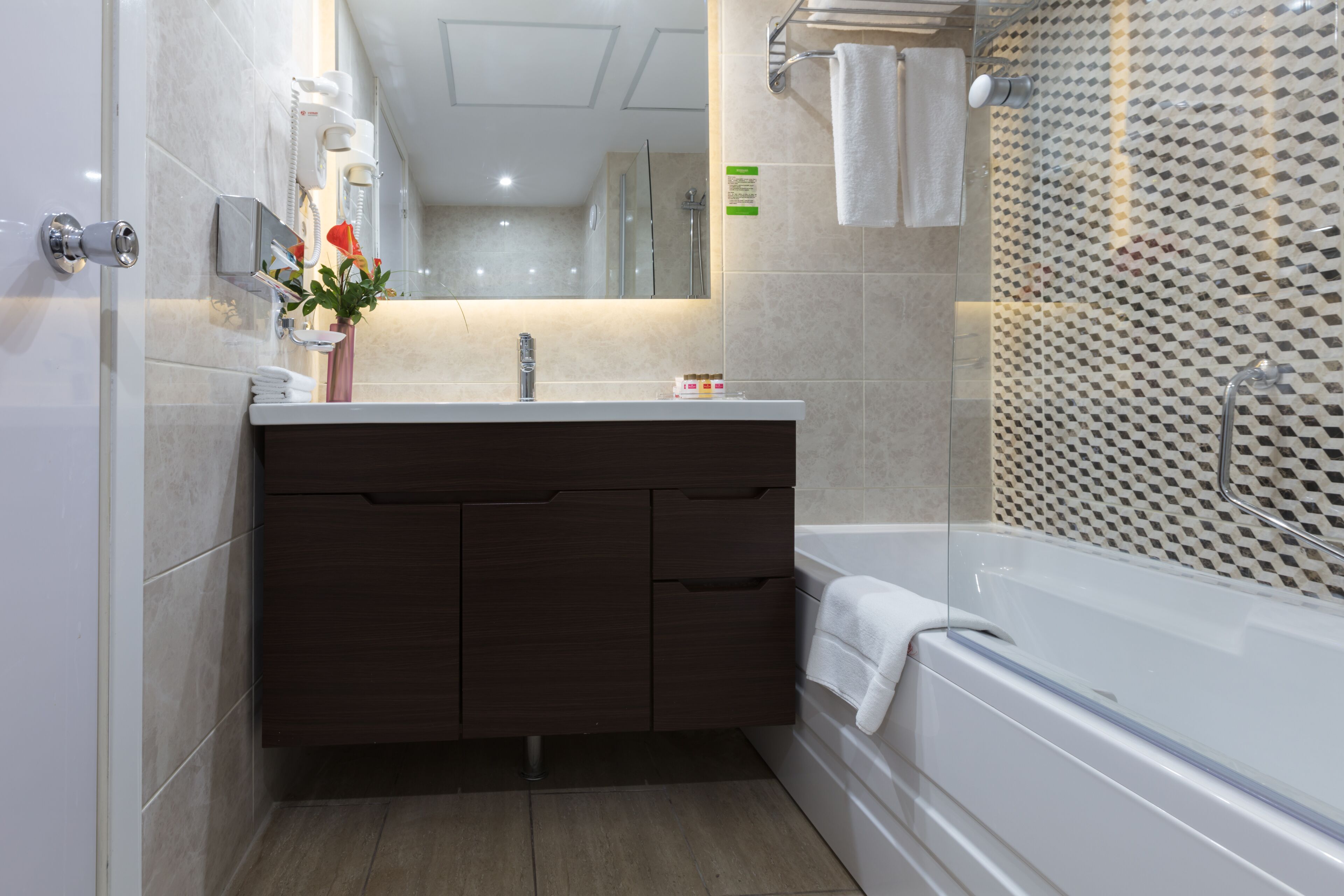 A modern bathroom with a dark wood vanity, a white bathtub, and a shower with a patterned glass door.
