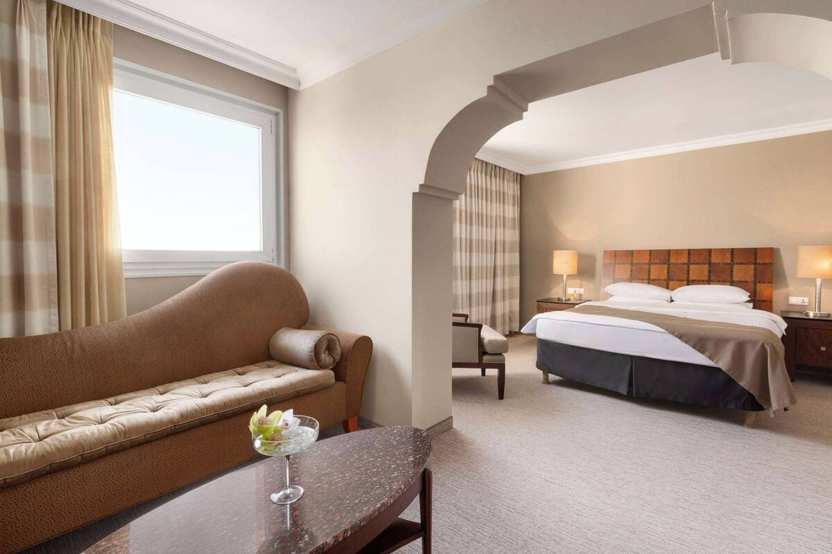 Une chambre d’hôtel avec un canapé, un lit, un bureau et une fenêtre avec des rideaux.