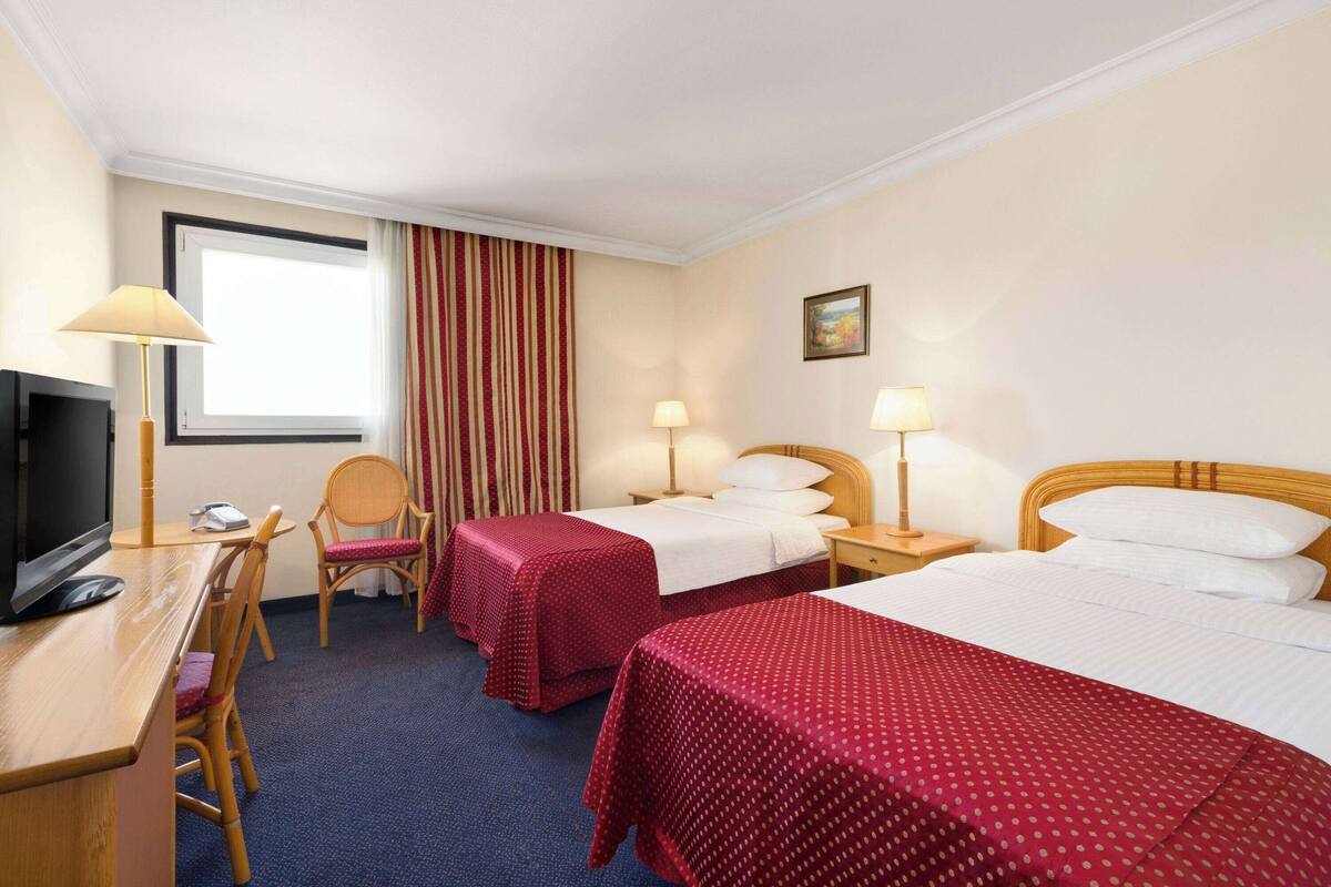 Une chambre d’hôtel avec deux lits, un bureau avec une télévision et une chaise.