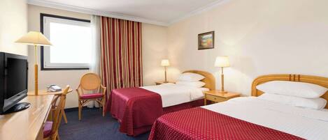 A hotel room with two beds, a desk with a TV, and a chair.