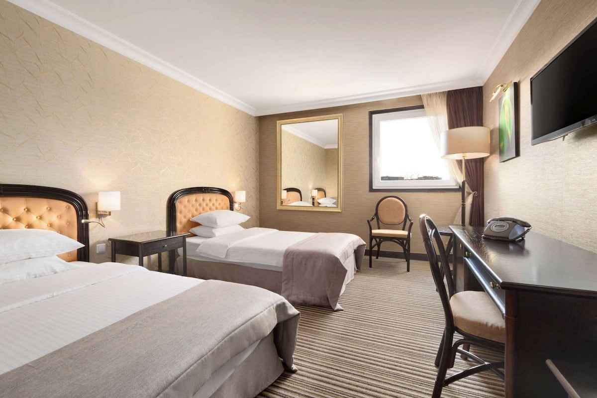 Une chambre d’hôtel avec deux lits, un bureau, une chaise, une télévision et un grand miroir.