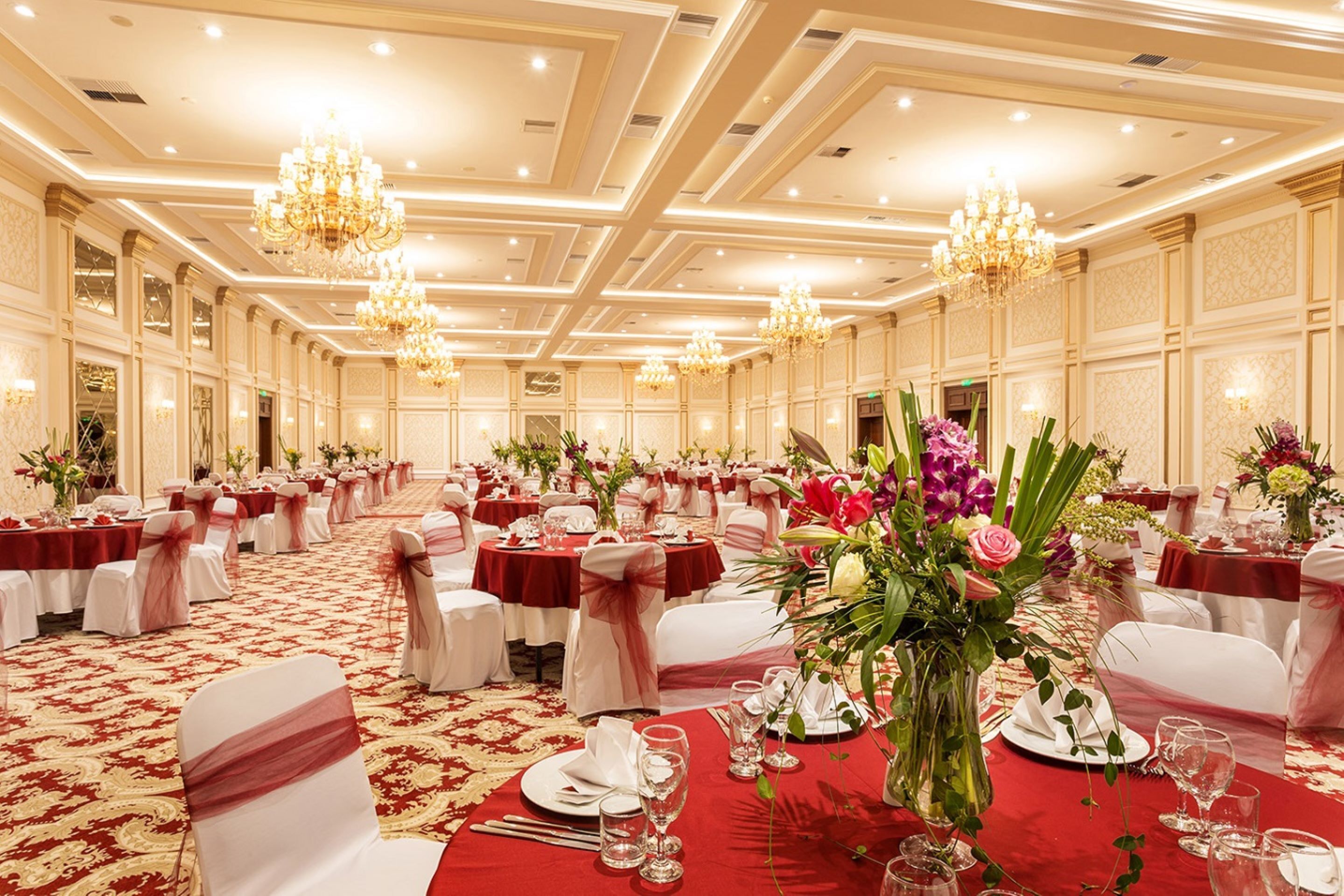 Un salón de banquetes con mesas redondas dispuestas para cenar, candelabros y centros de mesa florales.