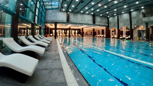 Ein Innenpool mit Liegestühlen am Rand, einer Glasdecke und einem modernen architektonischen Design.