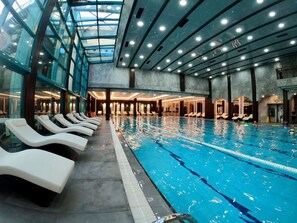 An indoor swimming pool with lounge chairs along the side, a glass ceiling, and a modern architectural design. - Ramada by Wyndham Sofia City Center (Sofia)
