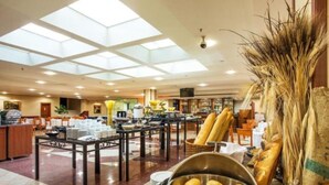Eine Hotelhalle mit hoher Decke, Oberlichtern, einem Frühstücksbereich mit Brot und einer Sitzecke mit Tischen und Stühlen.