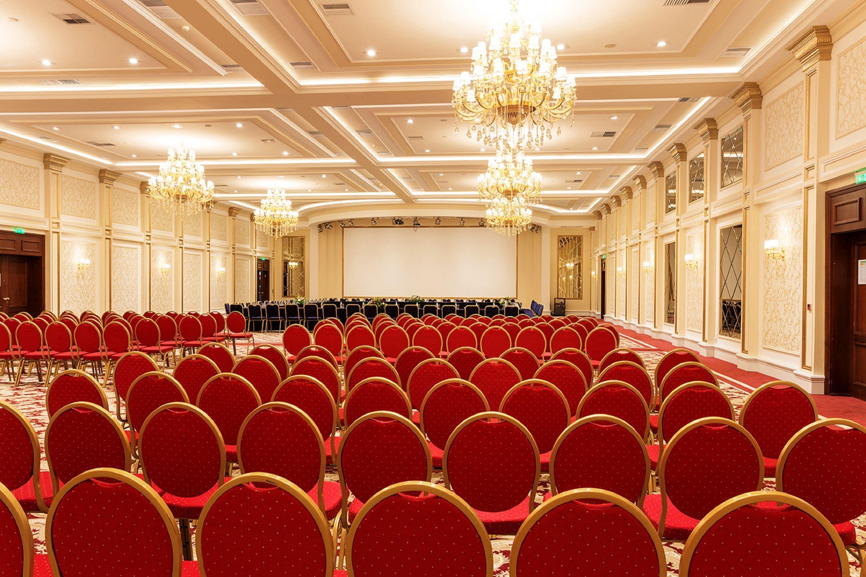 A large conference room with rows of red chairs and a stage.