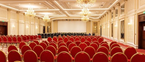 A large conference room with rows of red chairs and a stage.