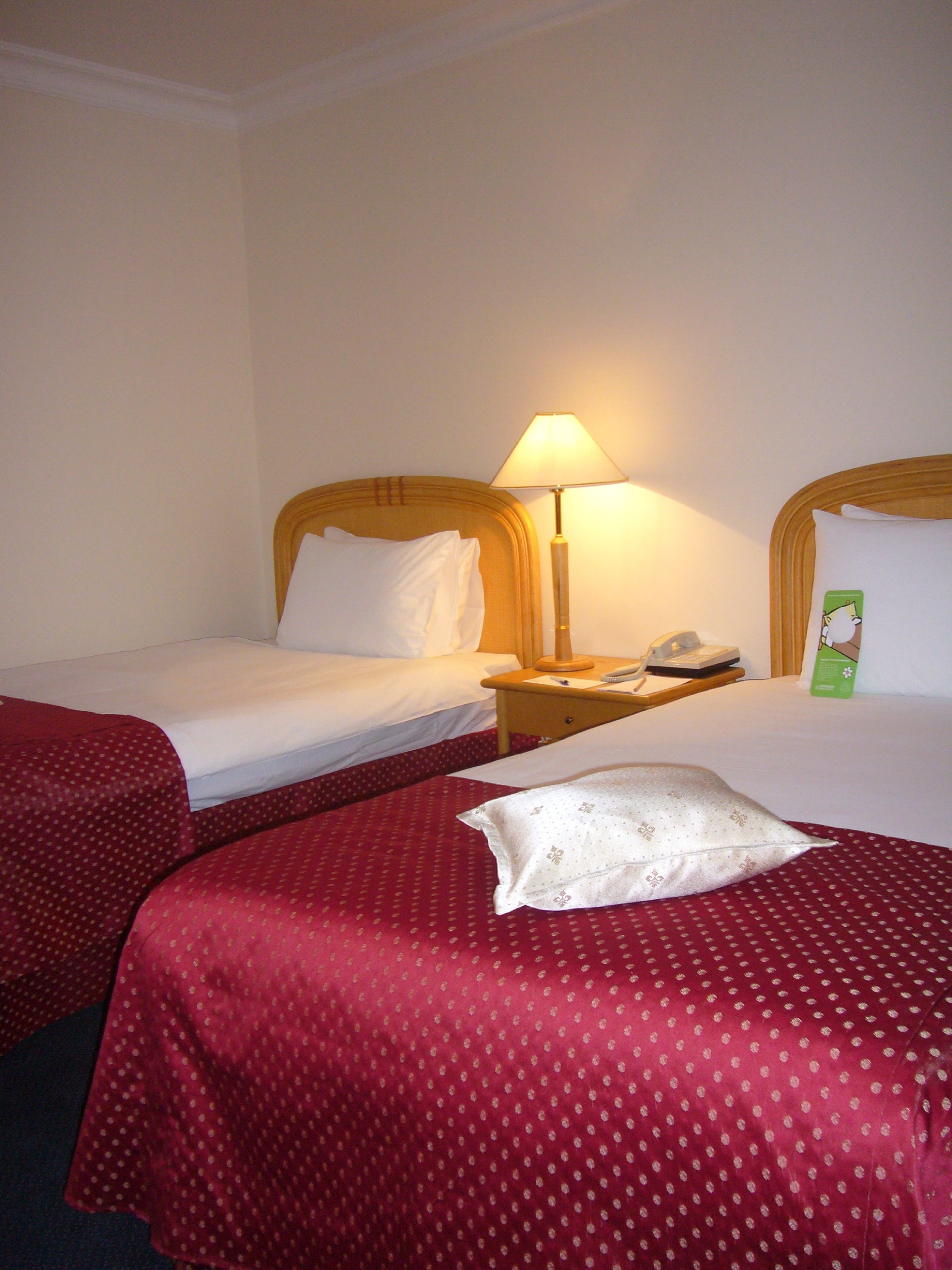 A hotel room with two single beds, each with a wooden headboard, a bedside table with a lamp, and a telephone.