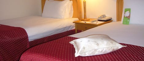 A hotel room with two single beds, each with a wooden headboard, a bedside table with a lamp, and a telephone.