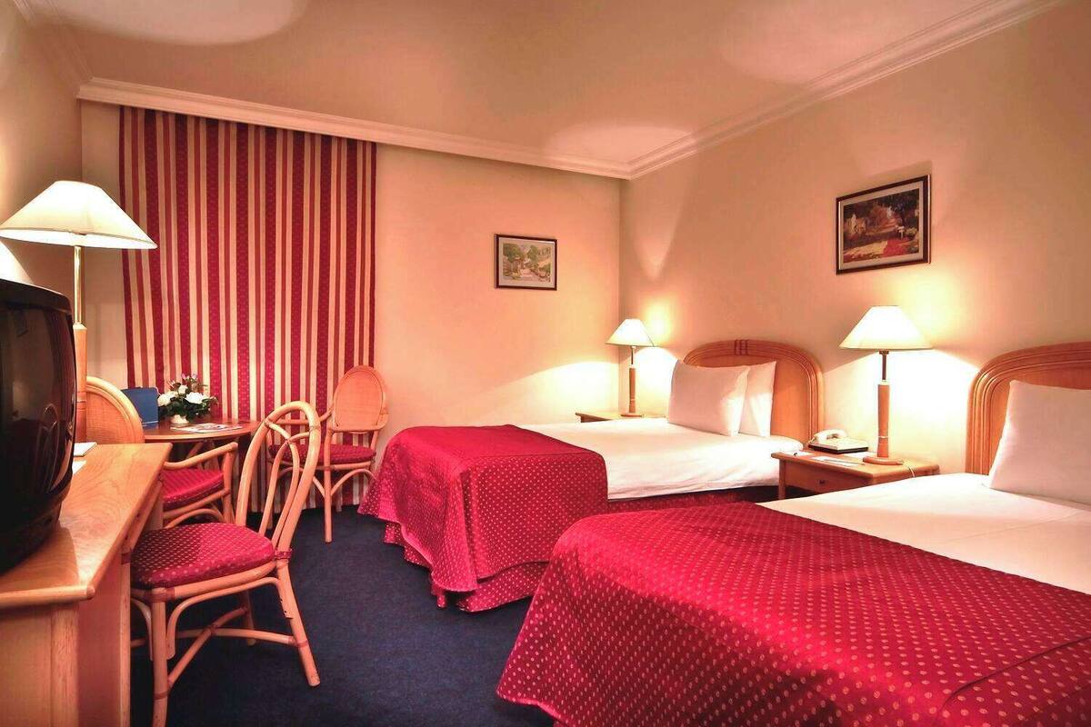 Une chambre d’hôtel avec deux lits, un bureau avec une chaise, une télévision et deux lampes.