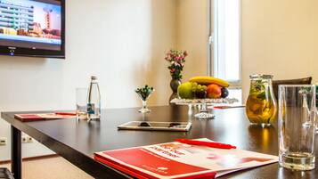 Una mesa de conferencias con una carpeta roja, un teléfono inteligente, una jarra de vidrio y un frutero.