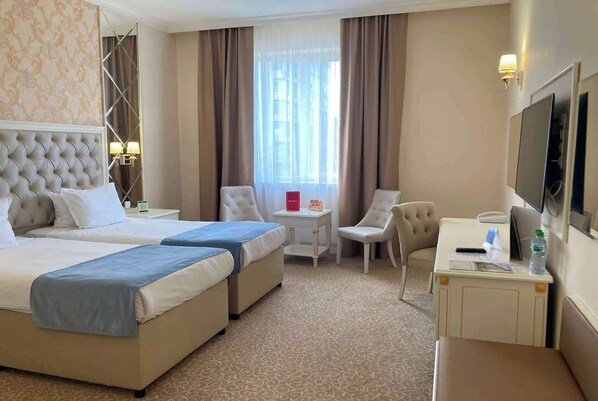 A hotel room with two beds, a desk, a chair, a TV, and a window with curtains.