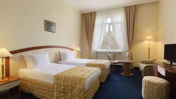 Et hotelværelse med to senge, et skrivebord, en stol, et fjernsyn og et vindue med gardiner.