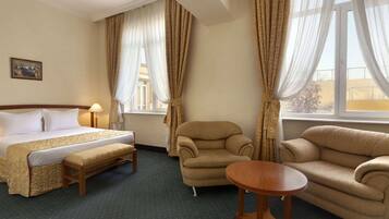 Una habitación de hotel con cama, sofá, silla, una mesita y cortinas.
