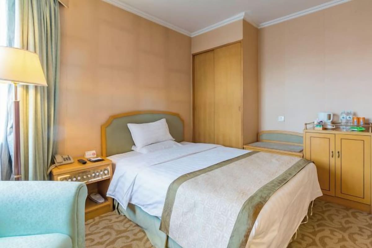 A hotel room with a bed, bedside table, lamp, and a wardrobe.