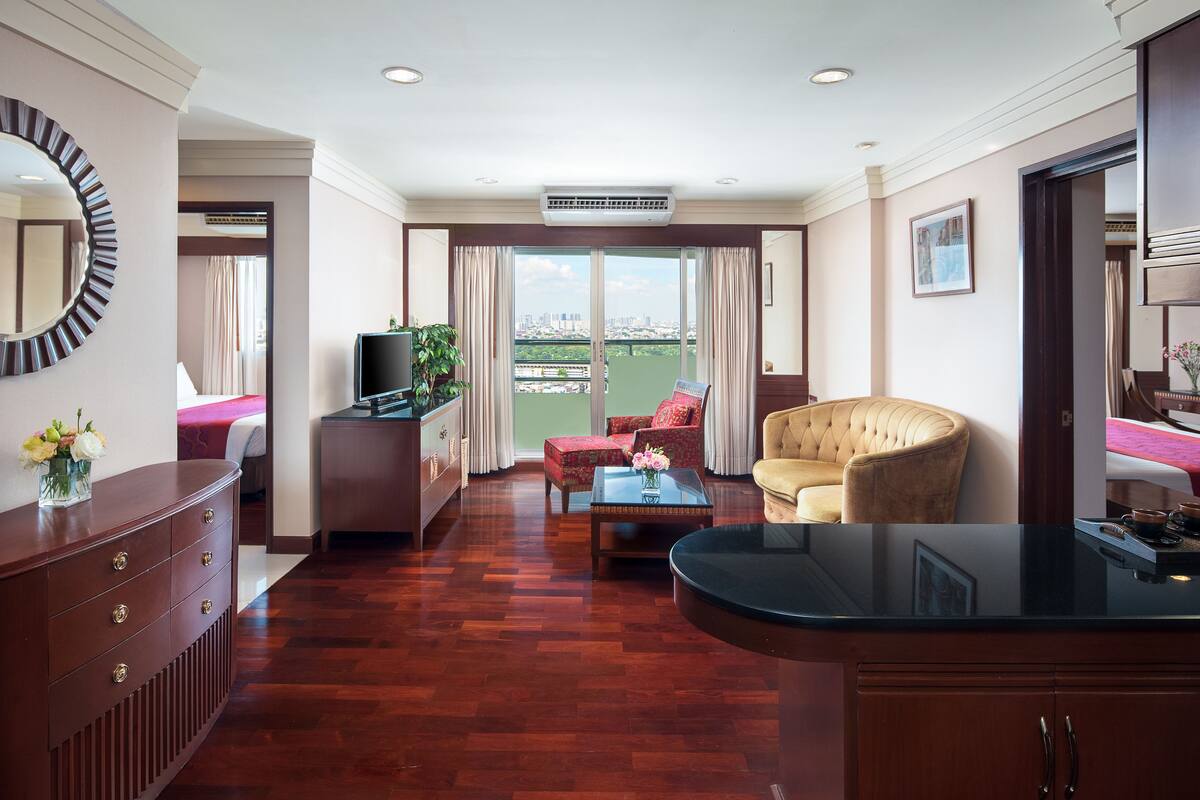 Ein Hotelzimmer mit Holzboden, einer Sitzecke, einem Sessel, einem Fernseher, einem Schreibtisch und einem Balkon mit Blick auf die Stadt.