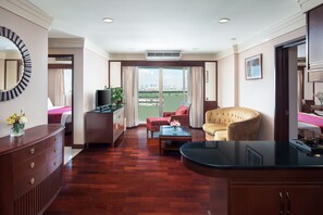 Habitación de hotel con piso de madera, un sofá, una silla, un televisor, un escritorio y un balcón con vista a la ciudad.