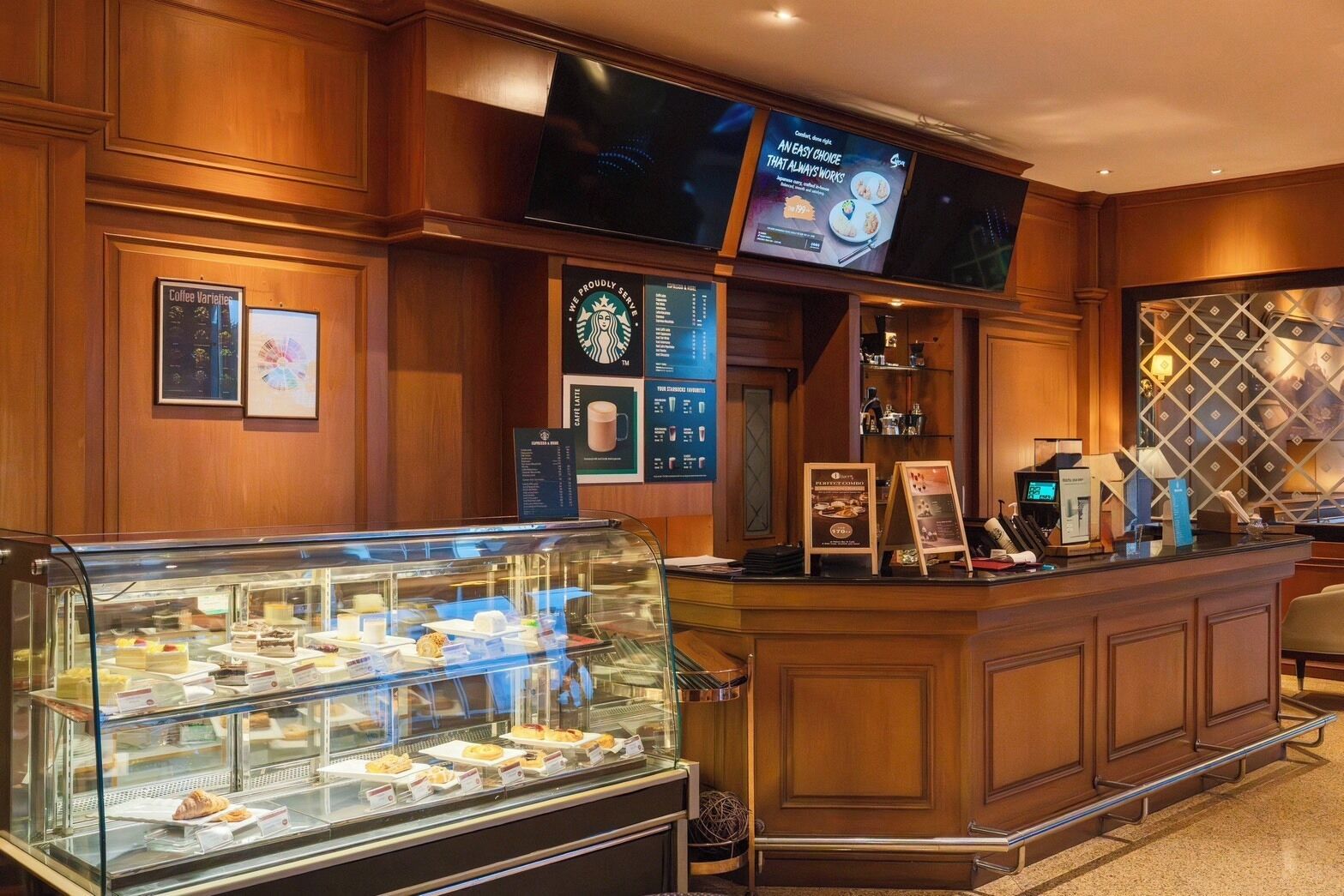 Un vestíbulo de hotel con una barra de café, una pantalla de televisión y una vitrina con pasteles.