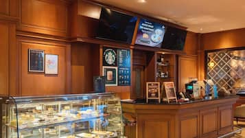 Un vestíbulo de hotel con una barra de café, una pantalla de televisión y una vitrina con pasteles.