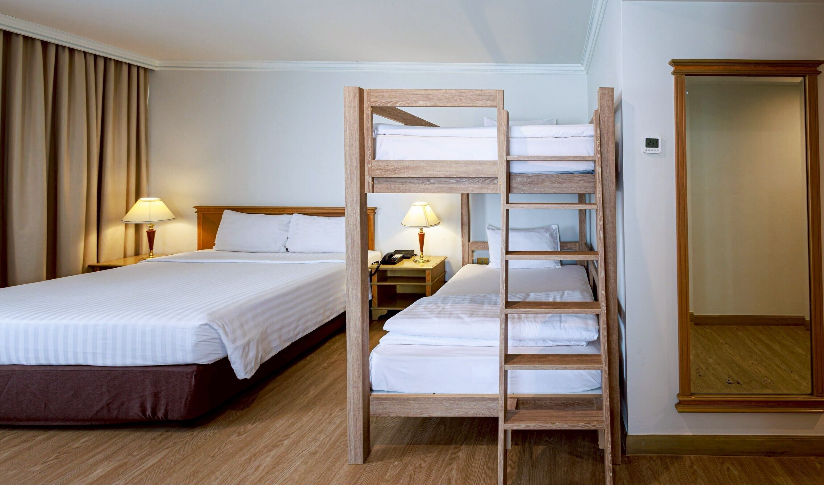 Una habitación de hotel con una cama litera, una mesita de noche con lámpara, un armario y un atril.