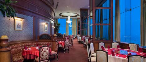 Un comedor formal con manteles blancos y rojos, sillas ornamentadas y vistas amplias a través de grandes ventanales.