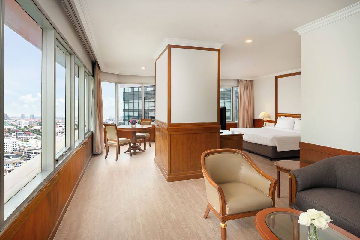 Ein Hotelzimmer mit großem Fenster, einem Bett, einem Schreibtisch, einem Sessel und einer Couch.