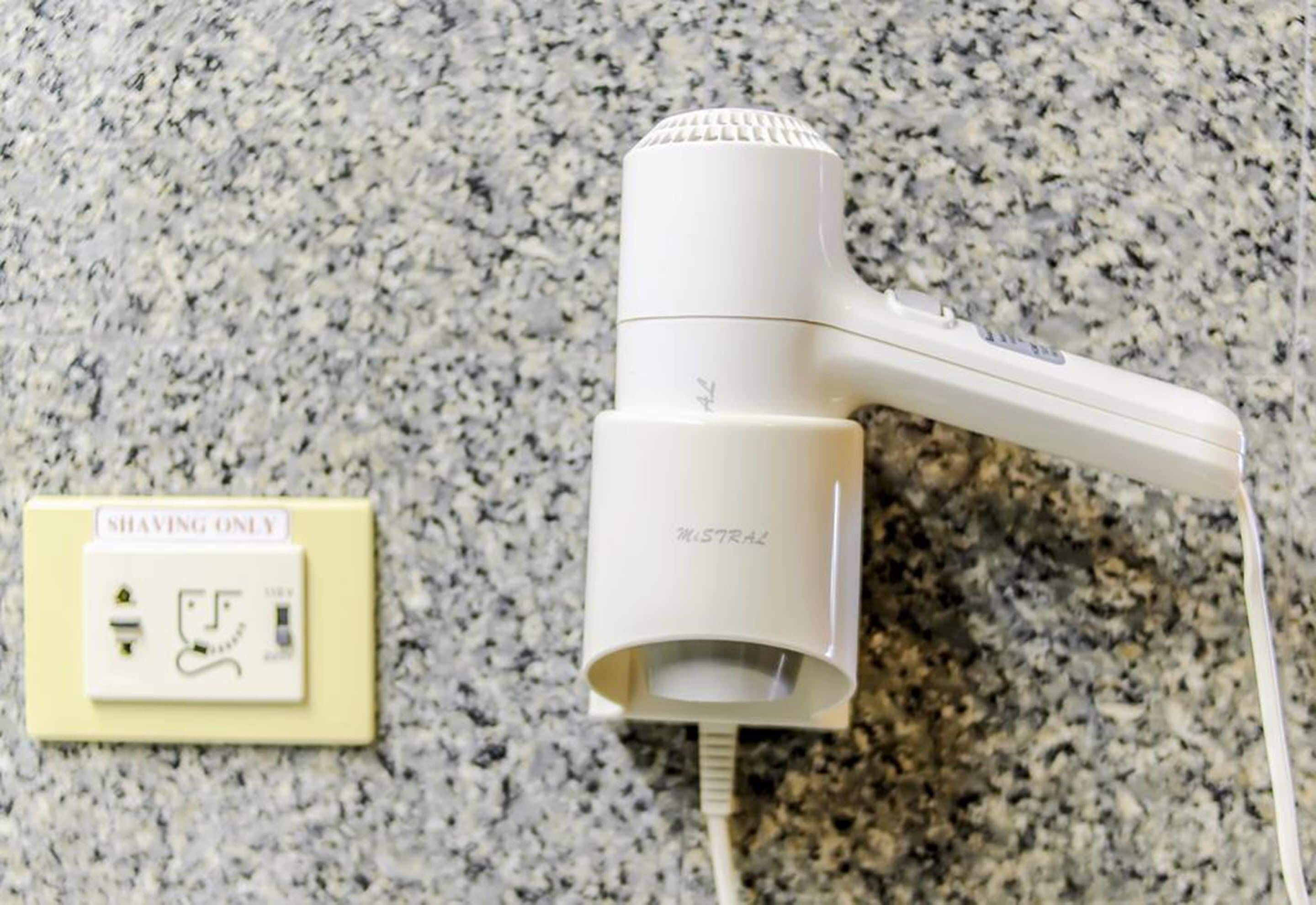 A hair dryer plugged into a wall socket with a switch labeled "SHAVING ONLY".