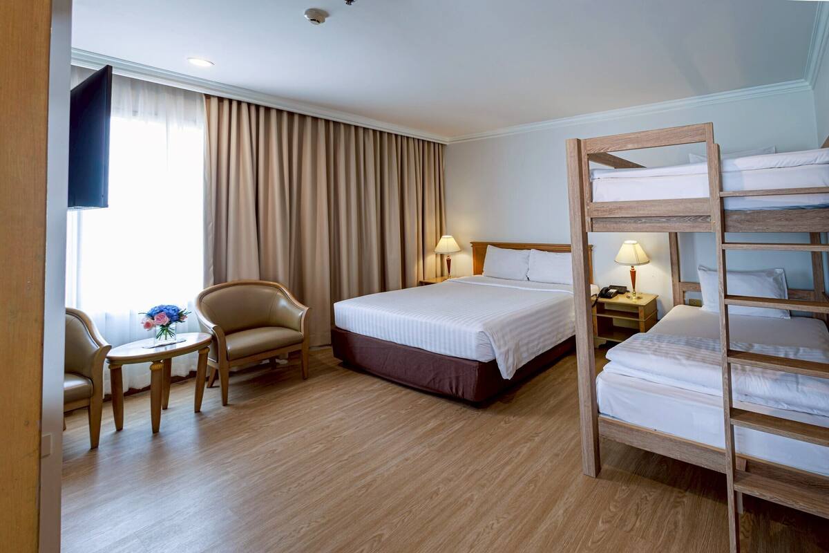 Ein Hotelzimmer mit einem großen Bett, einem hölzernen Etagenbett, einem Schreibtisch mit Stuhl, einem kleinen Tisch mit Blumen und einem Fernseher an der Wand.
