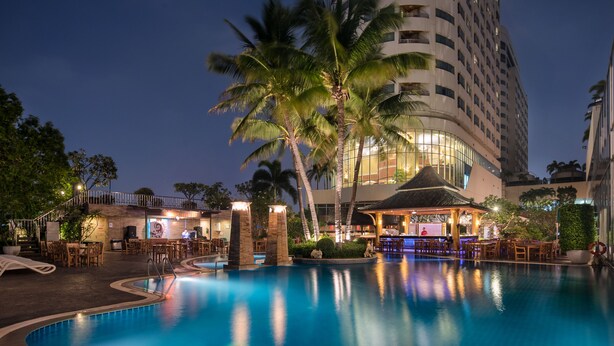 A nighttime pool area with a bar, lounge chairs, and palm trees. - Prince Palace Hotel Bangkok (Bangkok)